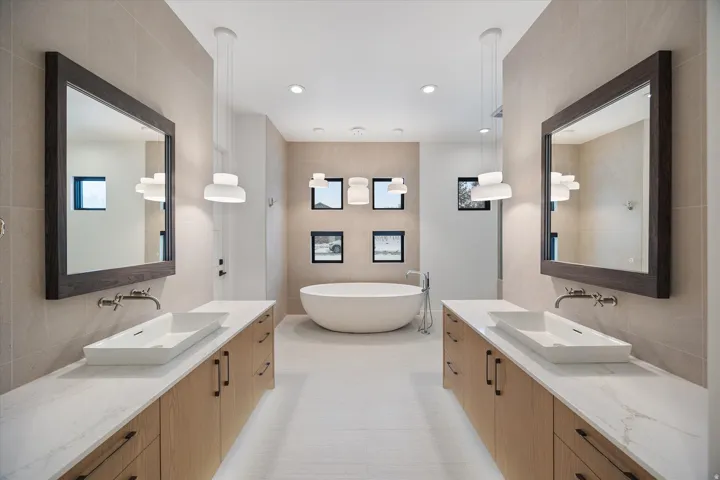 Full bath with tile walls, decorative backsplash, two vanities, a soaking tub, and recessed lighting