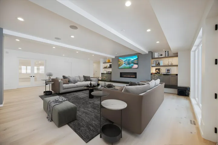 Living area with beam ceiling, light wood-type flooring, a warm lit fireplace, recessed lighting, and french doors