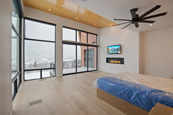 Bedroom featuring a glass covered fireplace, light wood-type flooring, ceiling fan, a high ceiling, and recessed lighting