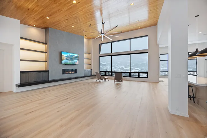 Unfurnished living room featuring a high wood ceiling, a large fireplace, a ceiling fan, light wood-type flooring, and recessed lighting