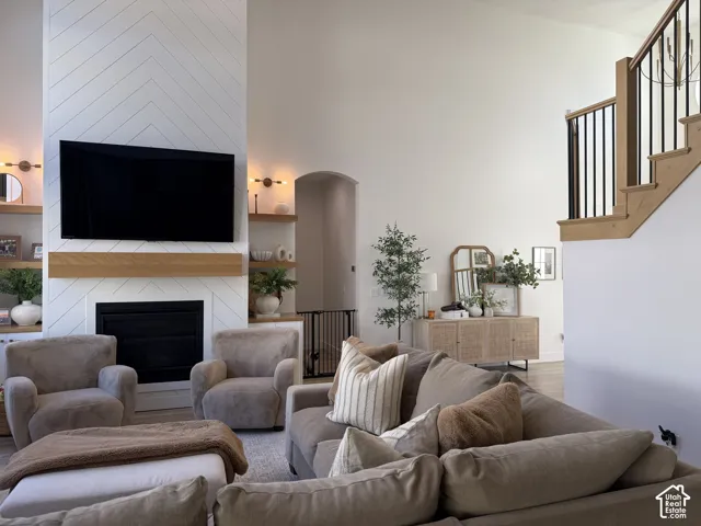 Open-concept living area showcasing a floor-to-ceiling fireplace with herringbone tile surround and black metal firebox, floating wood mantel with integrated shelving, and wall-mounted flat-screen TV