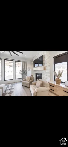 Stone-clad fireplace with a wood mantle, large black-framed windows, ceiling fan, recessed lighting, and wood-finish flooring