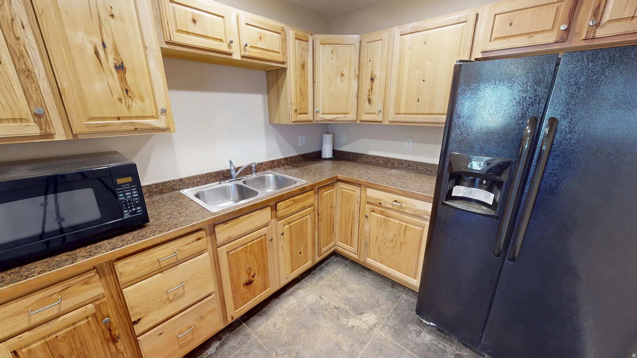 Kitchen featuring black appliances, light wood finish cabinets, and dark countertops