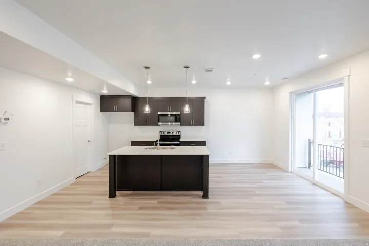 Open-concept living space featuring a kitchen island with pendant lighting, dark wood-finish cabinetry, built-in stainless steel appliances, and light wood-finish flooring