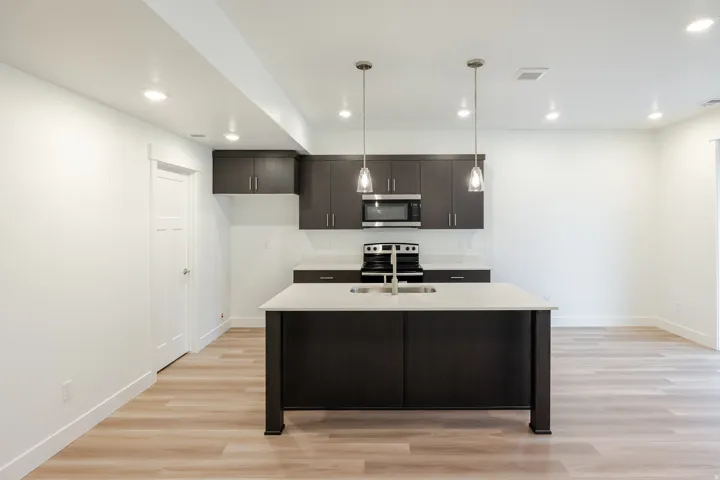 Open-concept kitchen featuring dark wood cabinetry, stainless steel appliances, a center island with sink, and pendant lighting