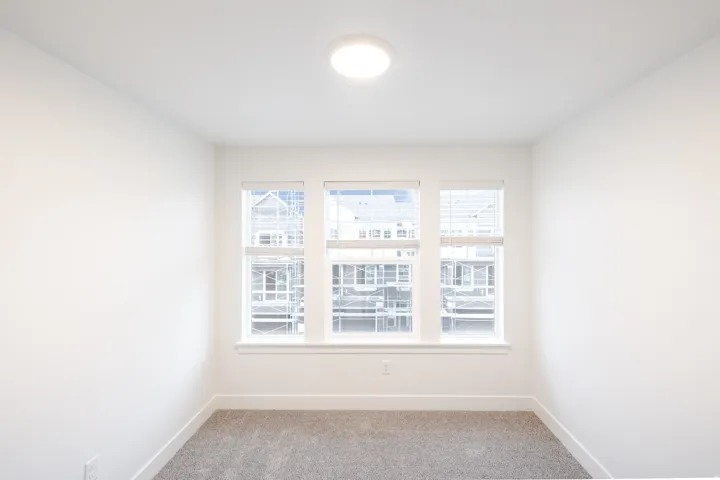 Room featuring triple windows with white blinds, neutral wall paint, gray carpet, and a flush-mount ceiling light