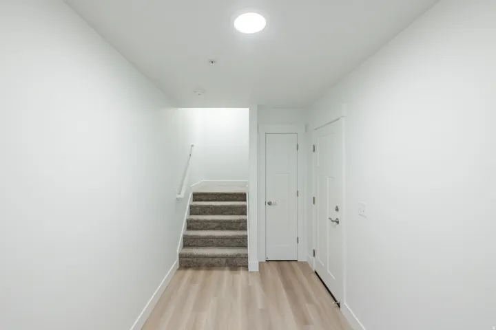 Bright hallway featuring light wood-finish flooring, white walls, a carpeted staircase with white handrail, and two paneled interior doors