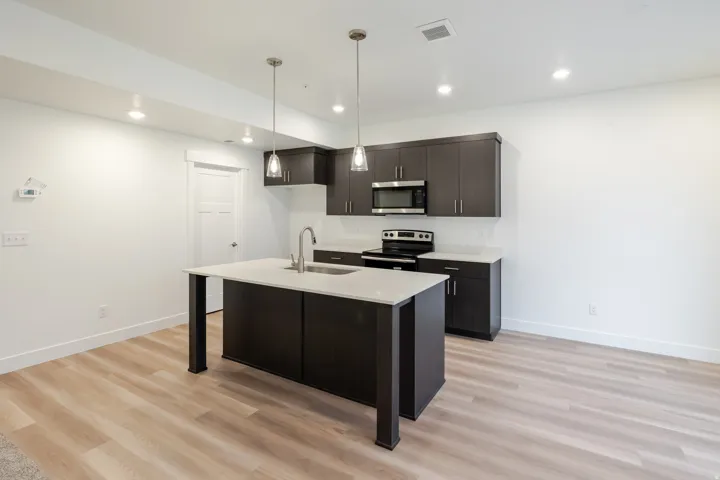 Kitchen featuring dark wood-finish cabinetry, light countertops, and a central island with an undermount sink