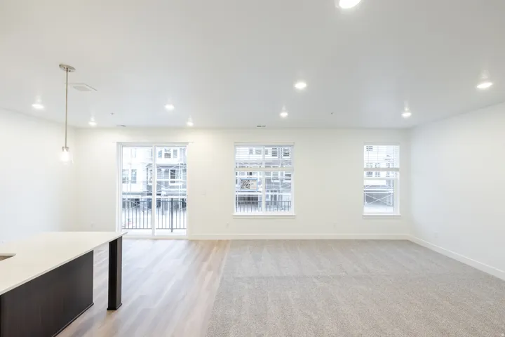 Open-concept living space featuring wood-finish flooring, recessed lighting, and a sliding glass door leading to a balcony