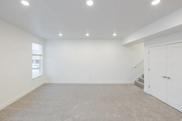Spacious room featuring neutral carpeting, white walls, recessed ceiling lighting, a window with blinds, and white bi-fold doors