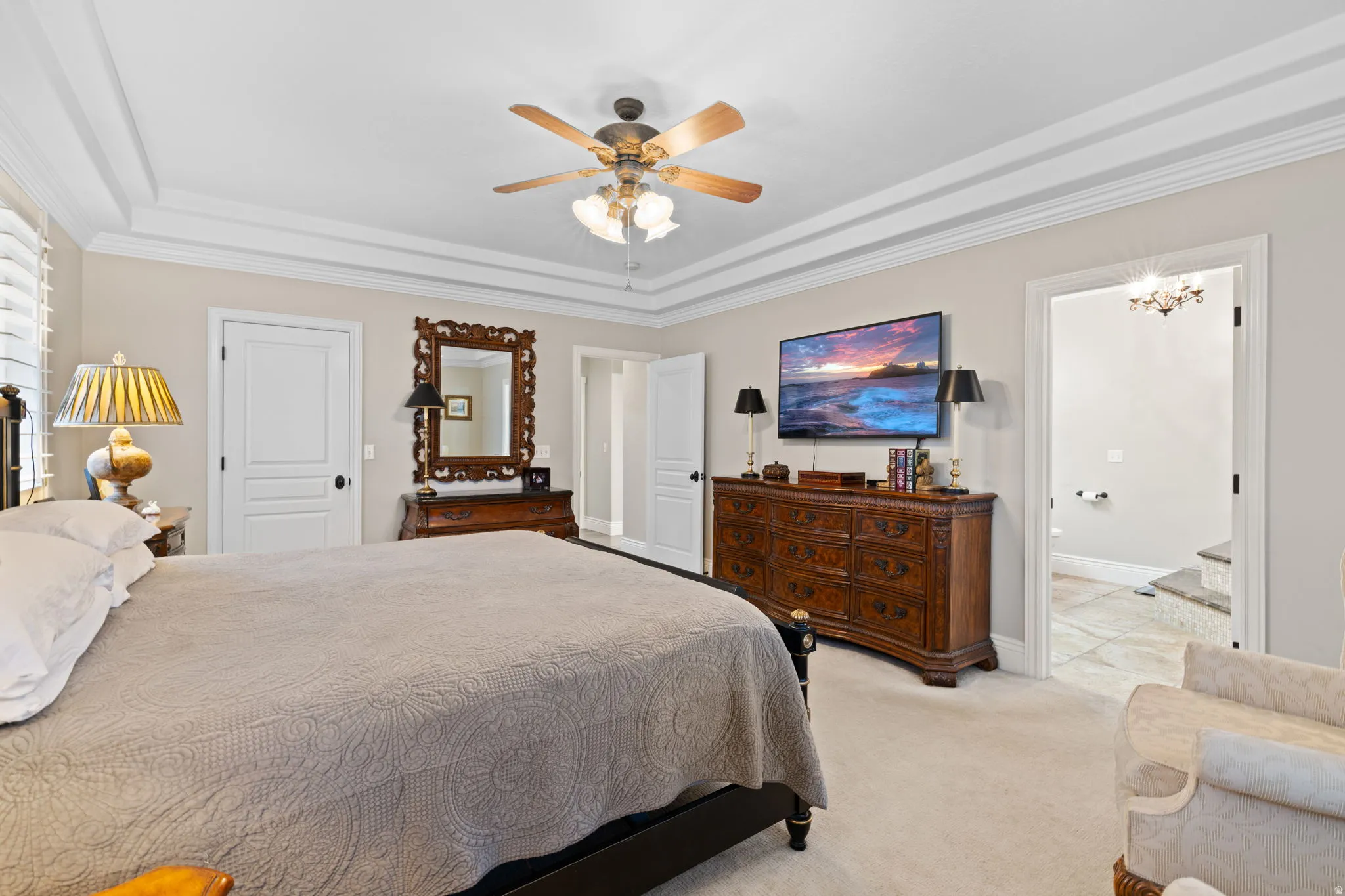 Bedroom with ceiling fan, a raised ceiling, light carpet, and ornamental molding