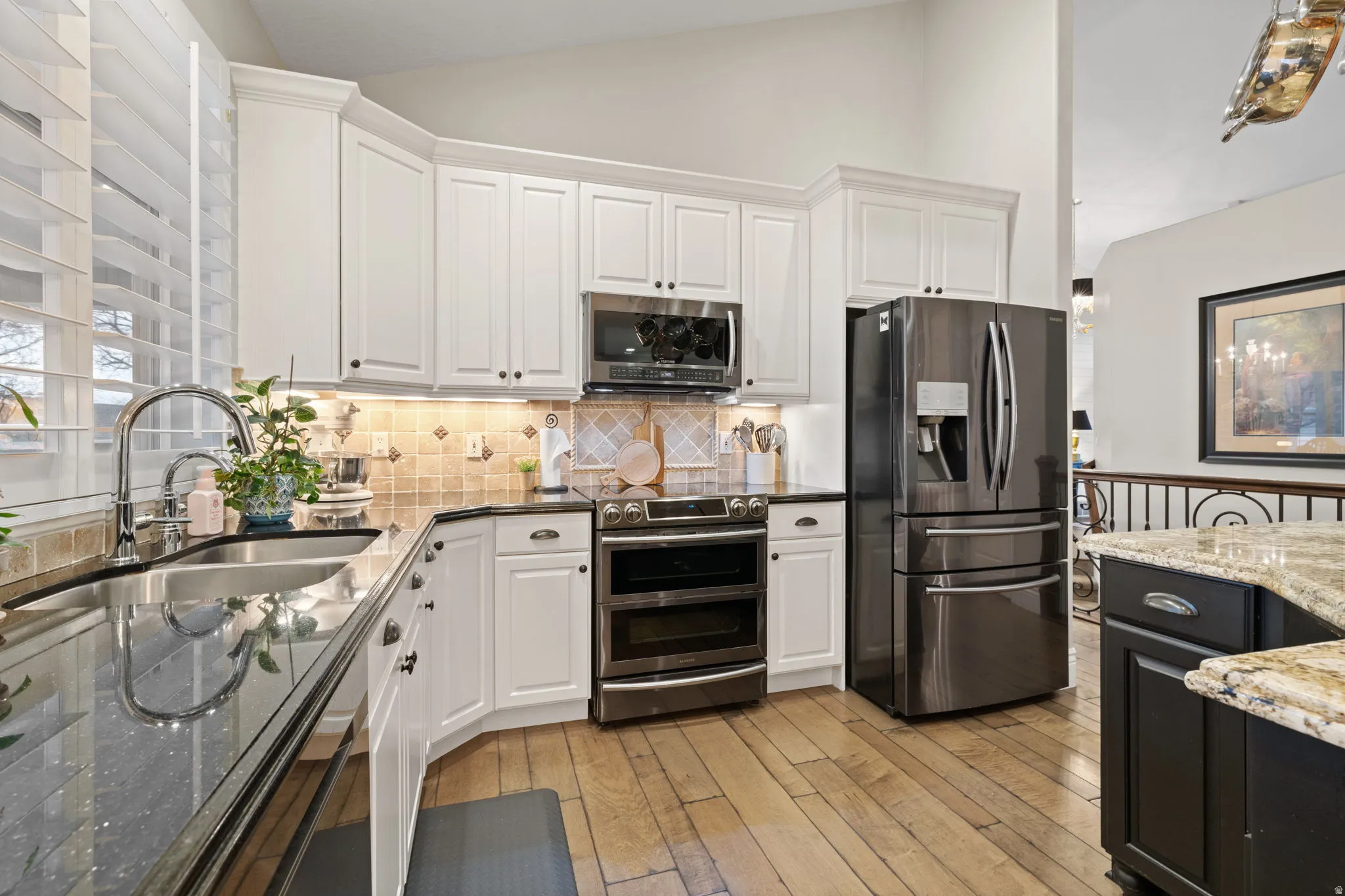 Dual tone kitchen with stainless steel appliances, dark stone counters, lofted ceiling, decorative backsplash, and light wood finished floors