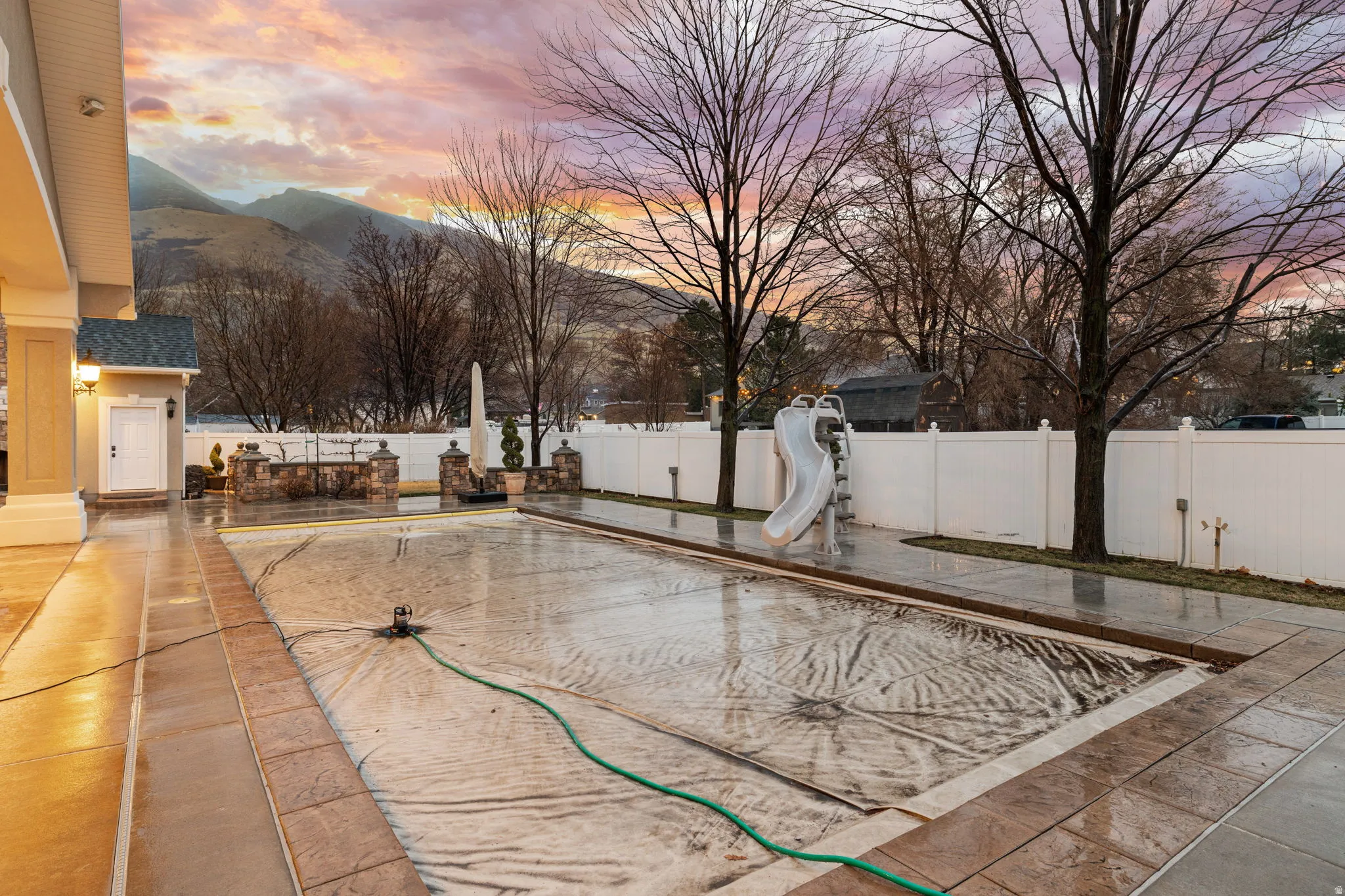 Pool at dusk with a patio, a fenced backyard, a water slide, and a mountain view