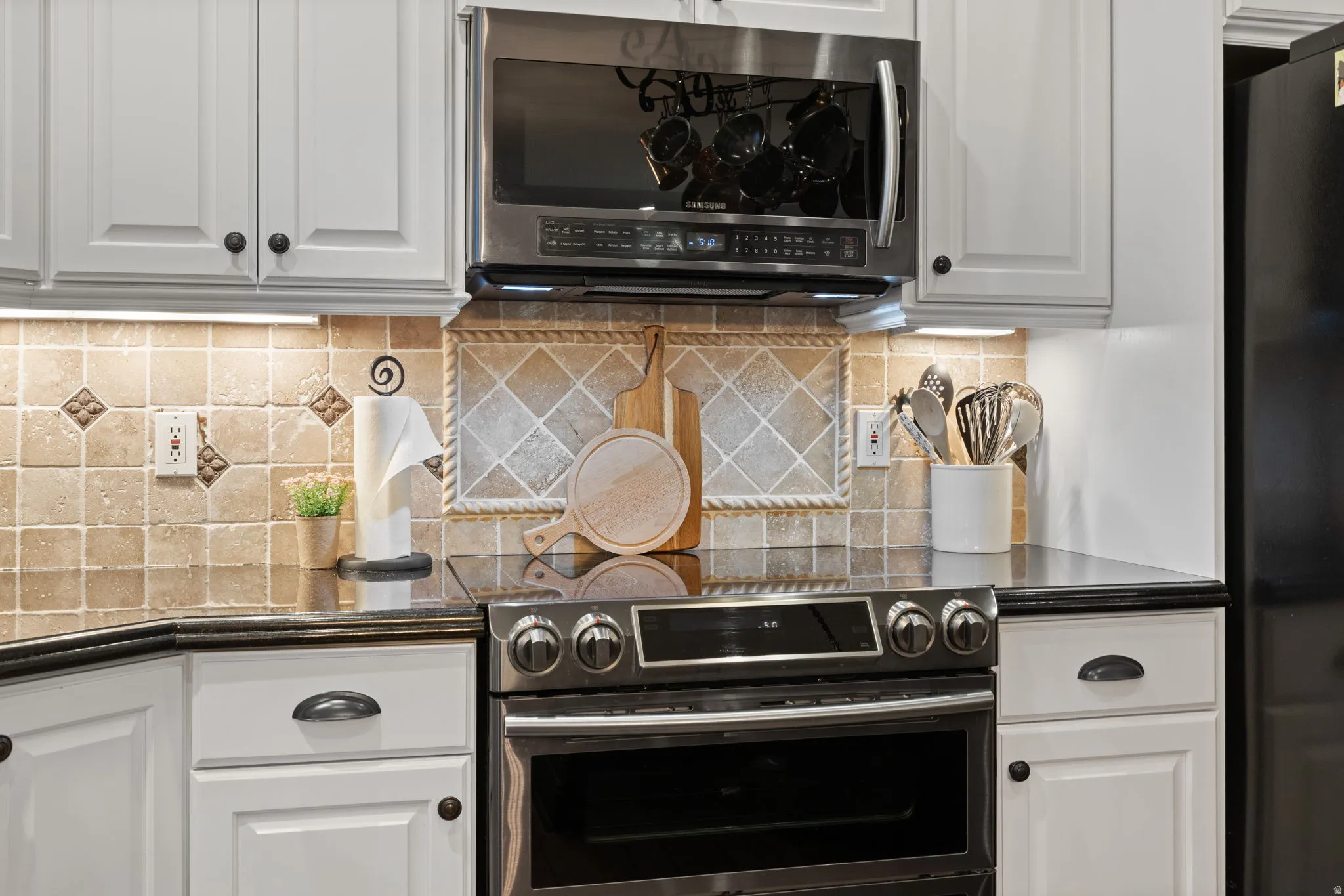 Kitchen with white cabinets, stainless steel appliances, tasteful backsplash, and dark stone countertops