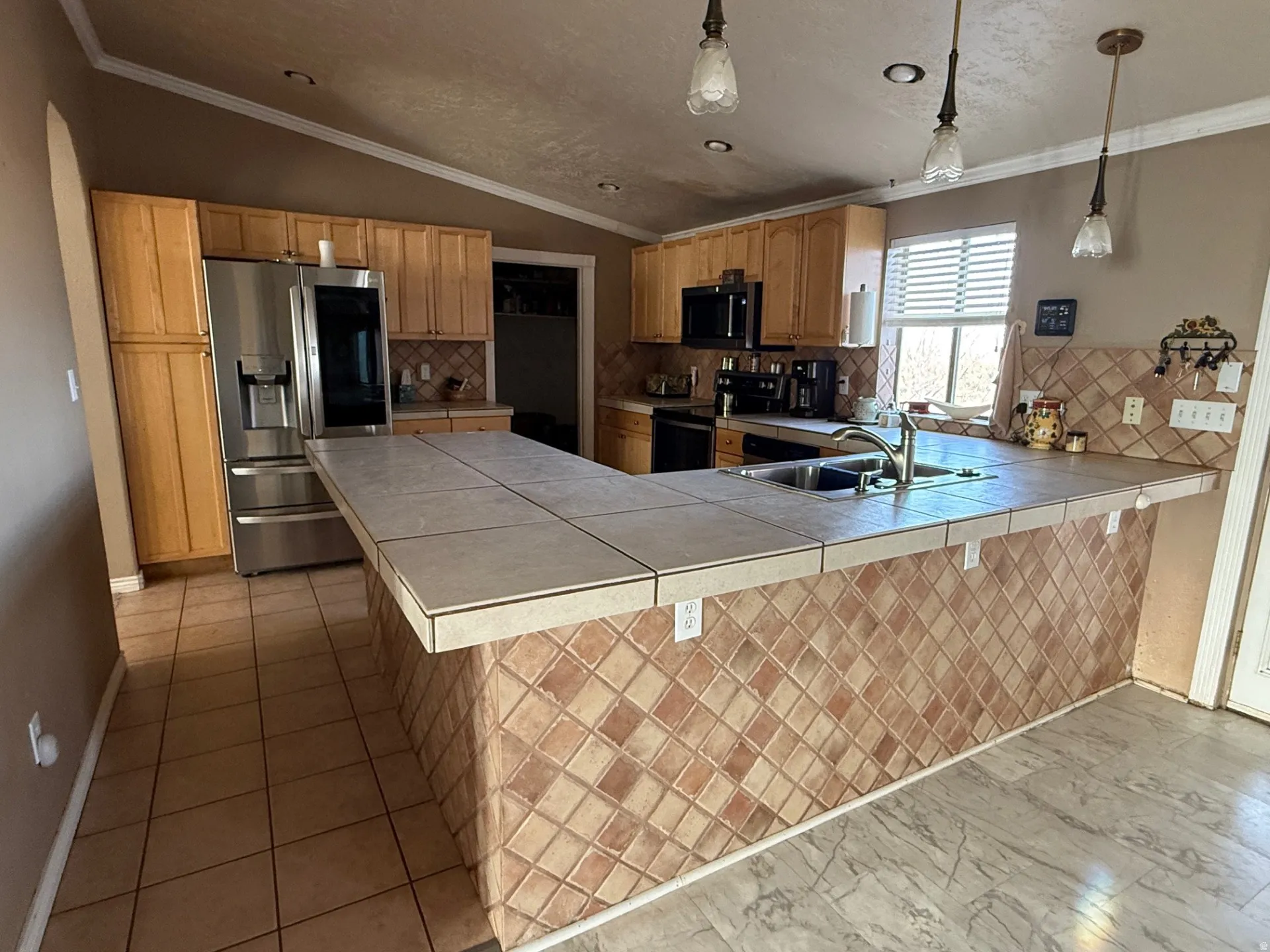 Kitchen featuring a peninsula, tile counters, ornamental molding, backsplash, and stainless steel appliances
