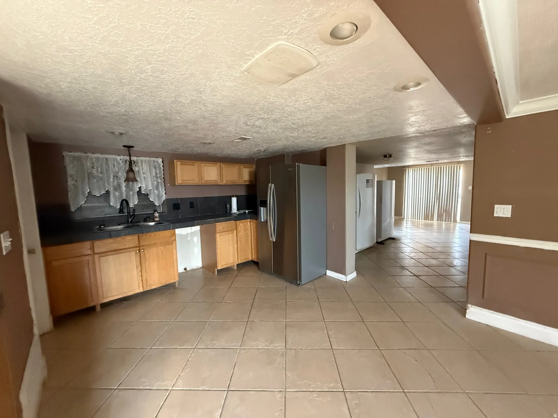 Kitchen with stainless steel fridge, light tile patterned floors, freestanding refrigerator, hanging light fixtures, and light wood finish cabinets
