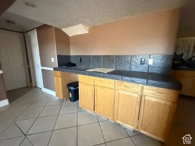 Kitchen with light tile patterned floors, tasteful backsplash, a textured ceiling, and light wood finish cabinets