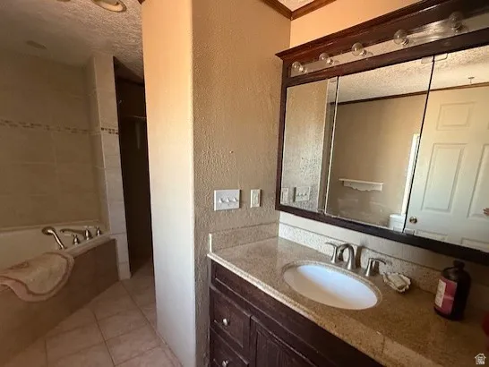 Full bathroom featuring vanity, a garden tub, a textured wall, light tile patterned floors, and a textured ceiling