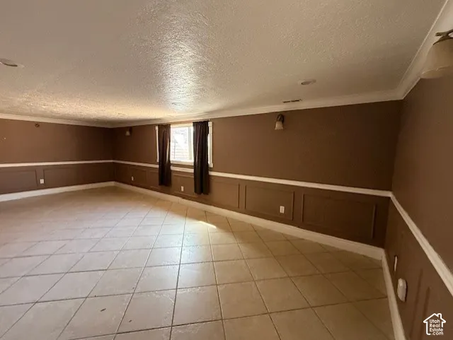 Spare room with wainscoting, a decorative wall, crown molding, a textured ceiling, and light tile patterned floors