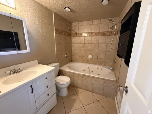 Full bath featuring a textured ceiling, vanity, a textured wall, a combined bath / shower with jetted tub, and light tile patterned floors