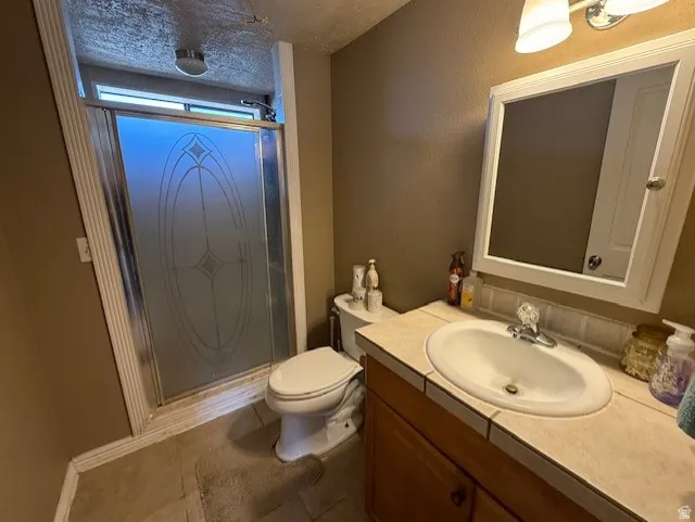 Full bathroom with vanity, a stall shower, a textured ceiling, and dark tile patterned flooring