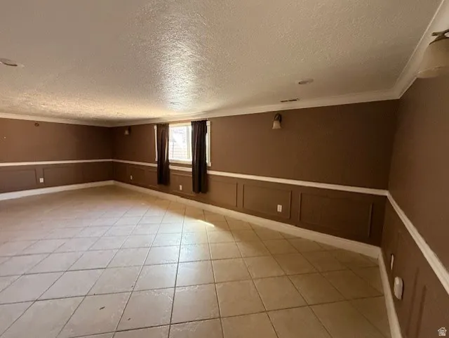Spare room with wainscoting, a decorative wall, crown molding, a textured ceiling, and light tile patterned floors
