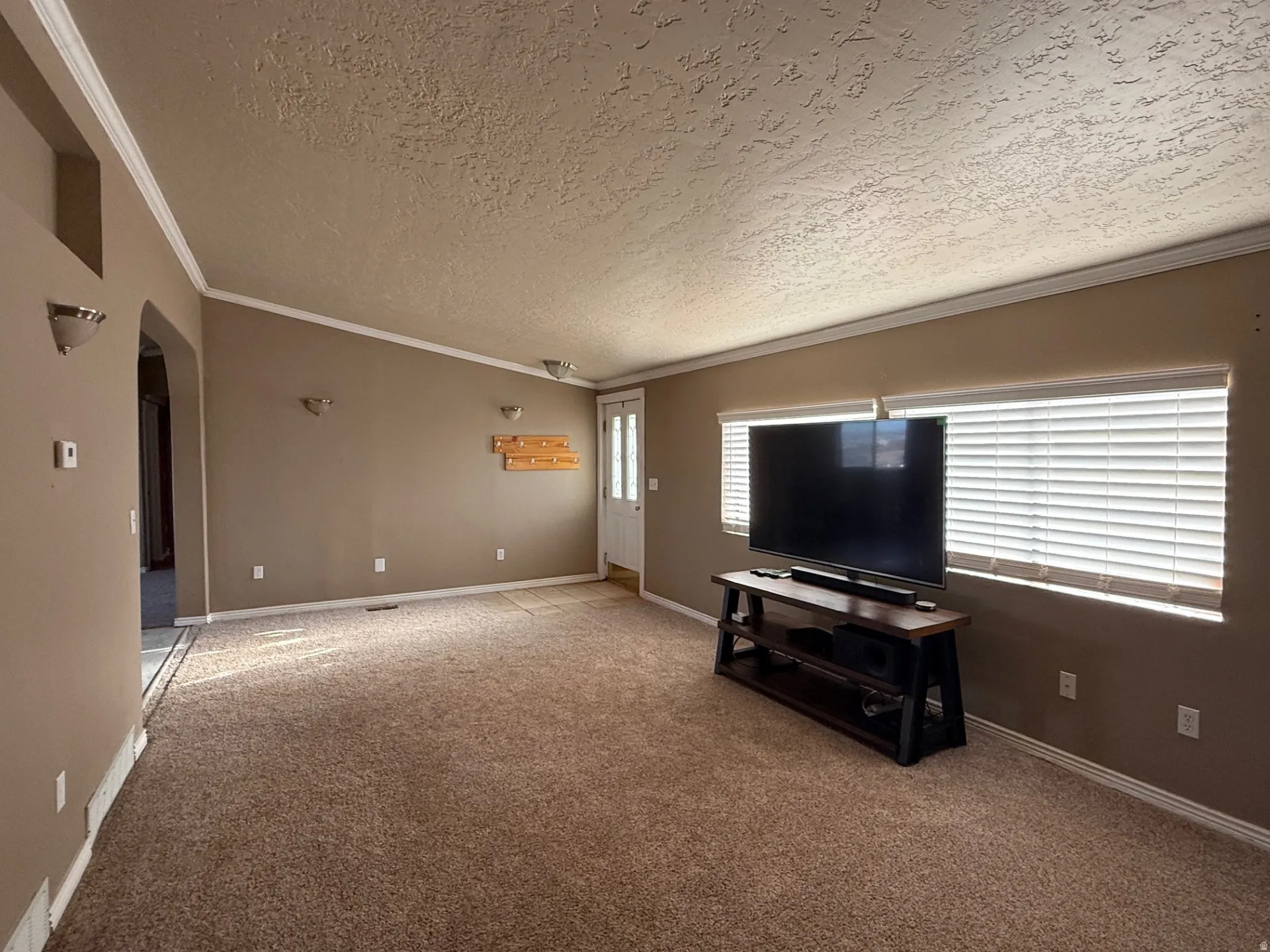 Unfurnished living room featuring arched walkways, light carpet, ornamental molding, and a textured ceiling
