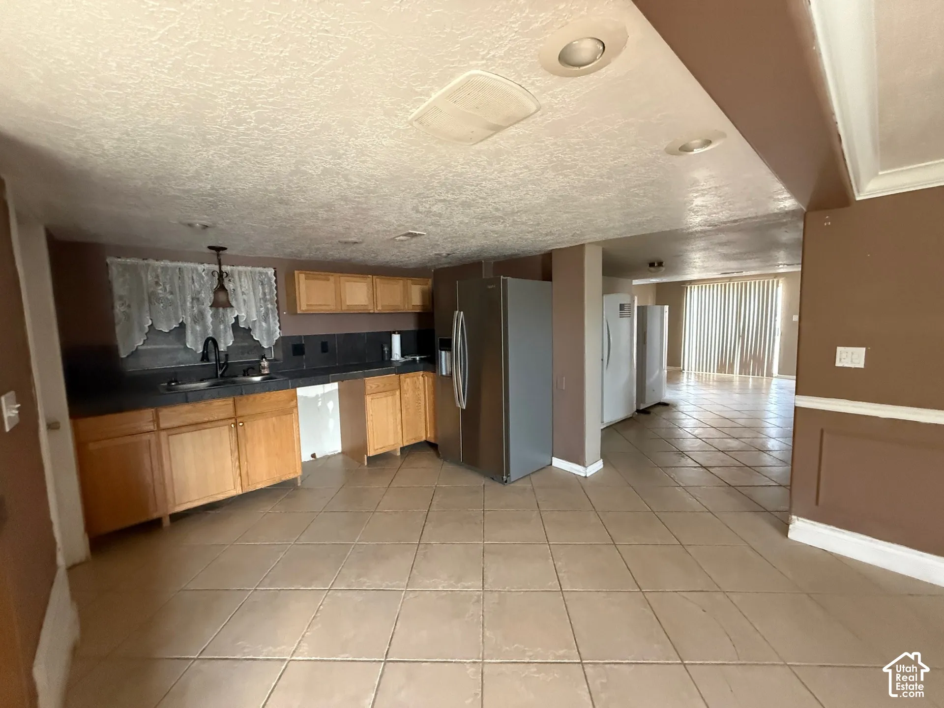 Kitchen with stainless steel fridge, light tile patterned floors, freestanding refrigerator, hanging light fixtures, and light wood finish cabinets