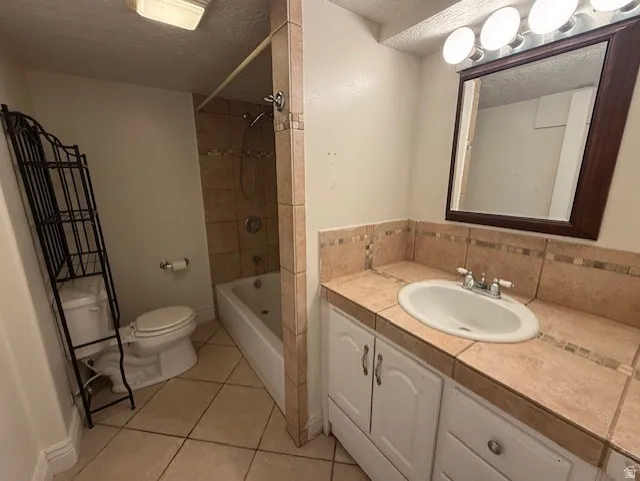 Bathroom featuring a textured ceiling, vanity, light tile patterned flooring, and bathtub / shower combination