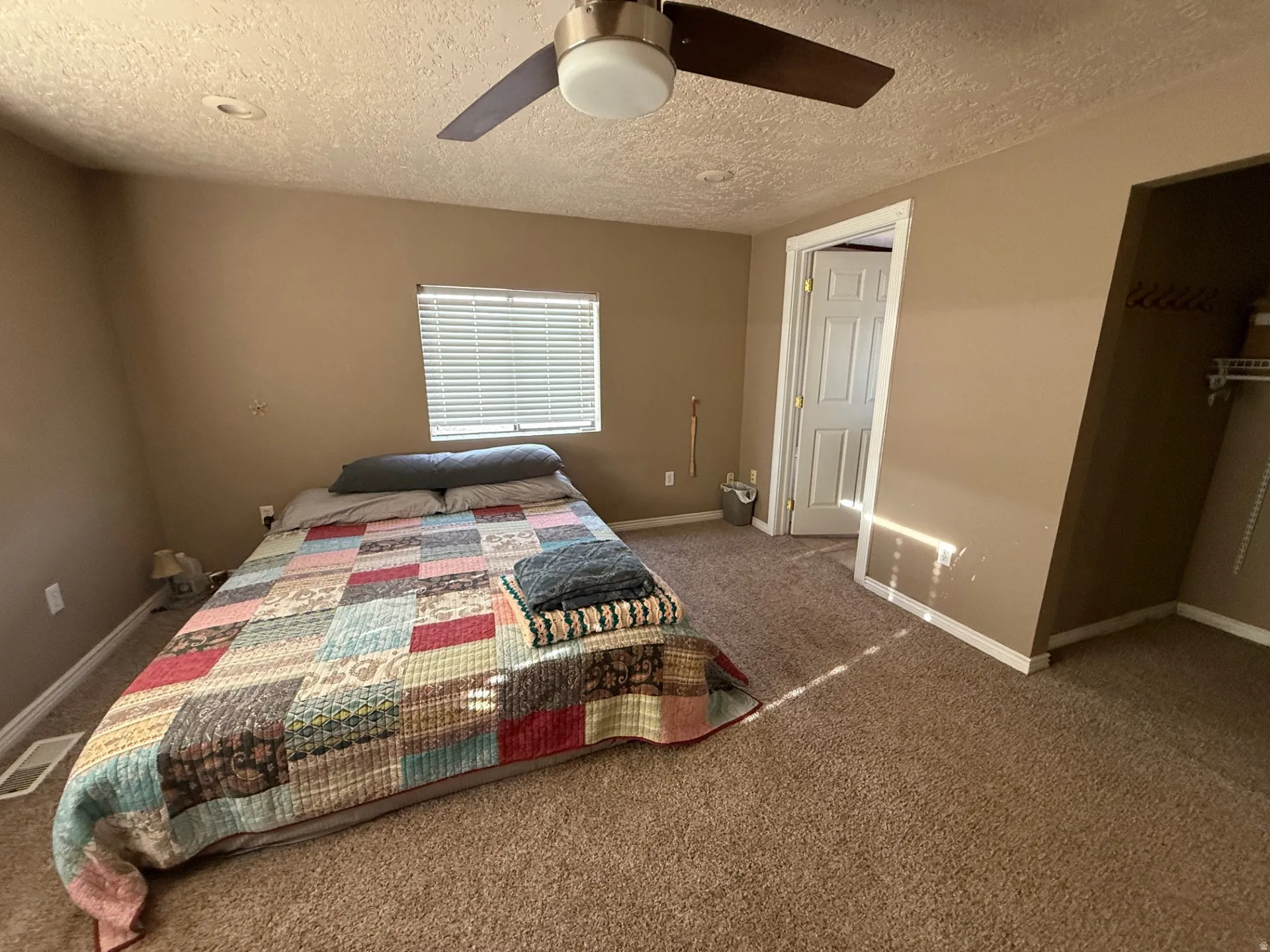 Carpeted bedroom featuring ceiling fan and a textured ceiling