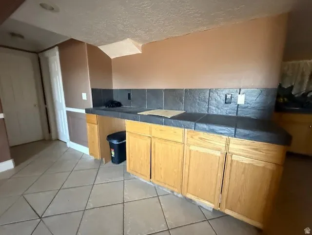 Kitchen with light tile patterned floors, tasteful backsplash, a textured ceiling, and light wood finish cabinets