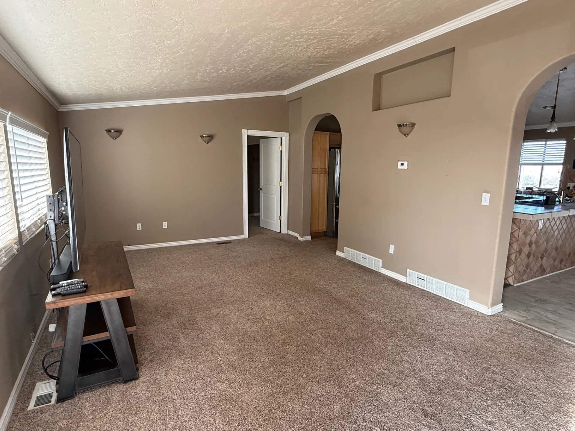 Unfurnished living room featuring arched walkways, light colored carpet, ornamental molding, and a textured ceiling