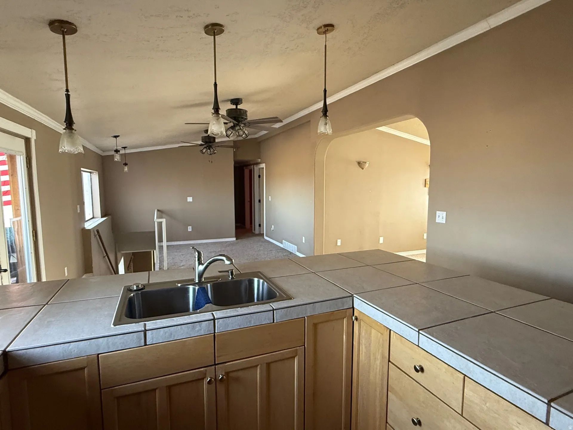 Kitchen featuring ornamental molding, a ceiling fan, arched walkways, open floor plan, and pendant lighting