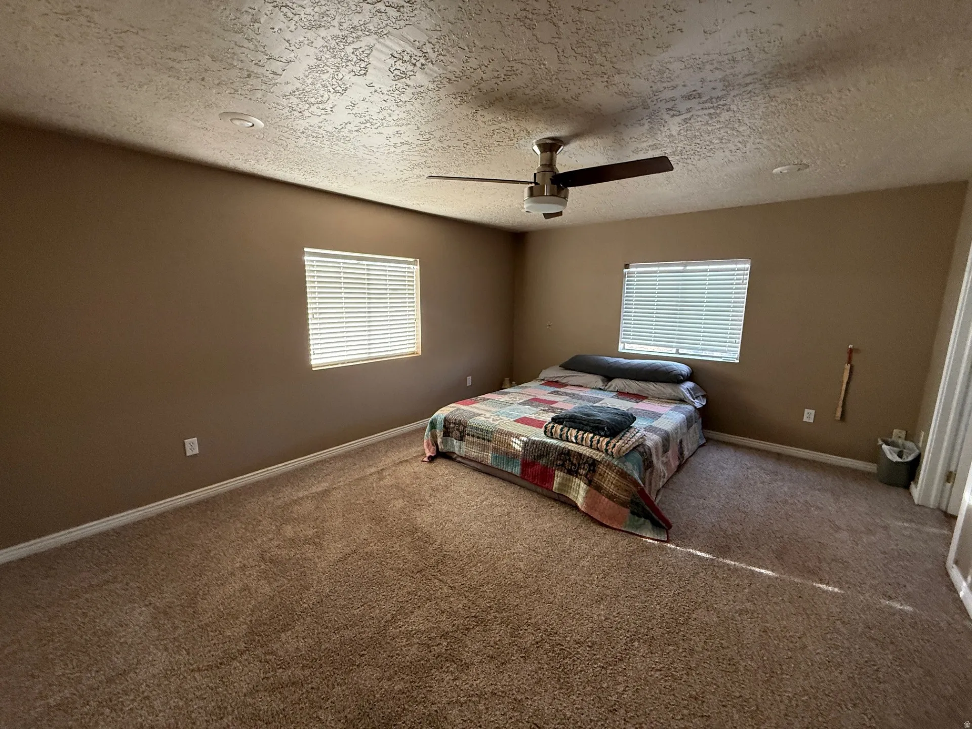 Carpeted bedroom with ceiling fan, multiple windows, and a textured ceiling