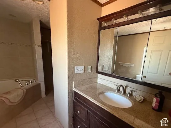 Full bathroom featuring vanity, a garden tub, a textured wall, light tile patterned floors, and a textured ceiling