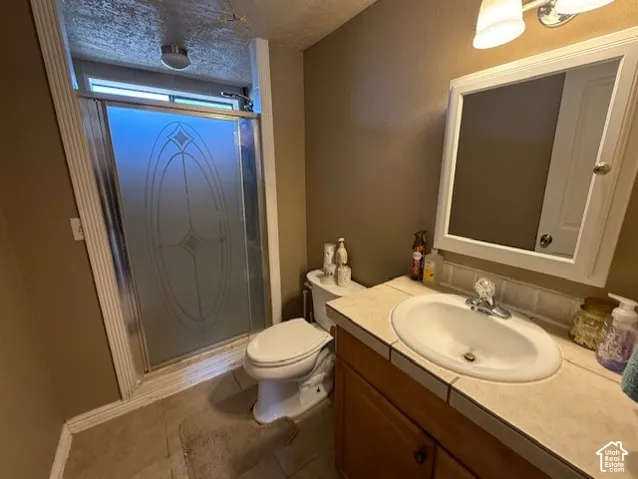 Full bathroom with vanity, a stall shower, a textured ceiling, and dark tile patterned flooring