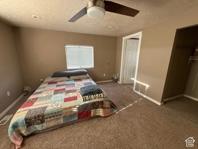 Carpeted bedroom featuring ceiling fan and a textured ceiling