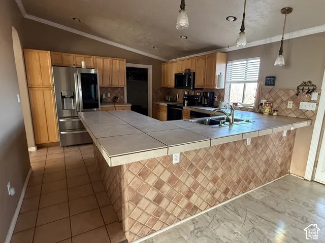 Kitchen featuring a peninsula, tile counters, ornamental molding, backsplash, and stainless steel appliances