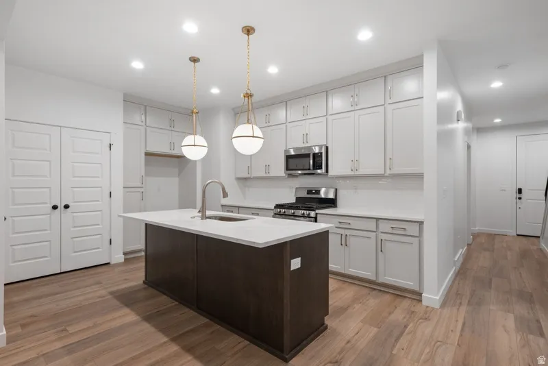 Dual tone kitchen with a center island with sink, two tone cabinetry, stainless steel appliances, dark wood-style flooring, and decorative light fixtures