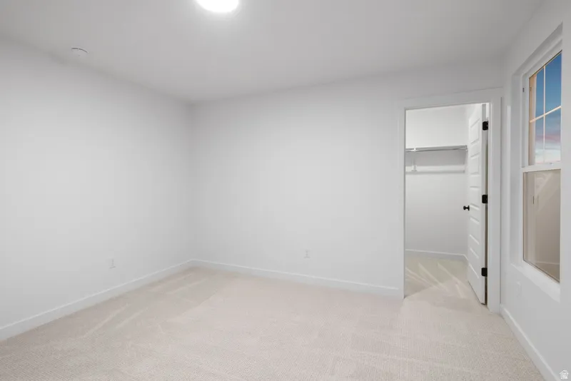 Unfurnished bedroom with a spacious closet and light colored carpet