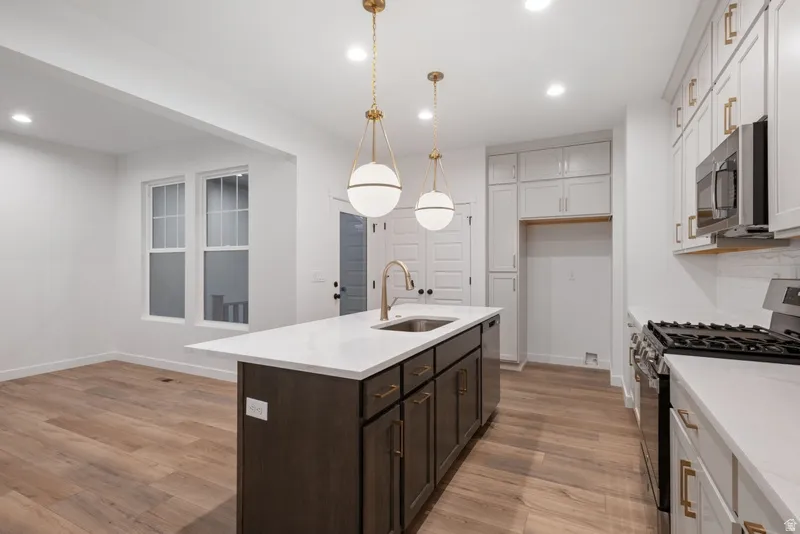 Kitchen featuring stainless steel appliances, light stone countertops, a kitchen island with sink, light wood-style floors, and pendant lighting