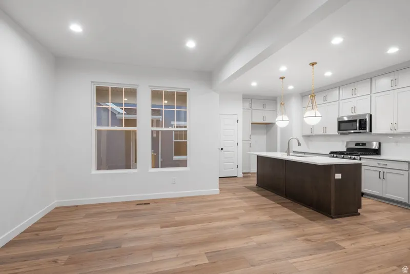 Kitchen with two tone color scheme, a center island with sink, stainless steel appliances, light wood-style floors, and decorative light fixtures