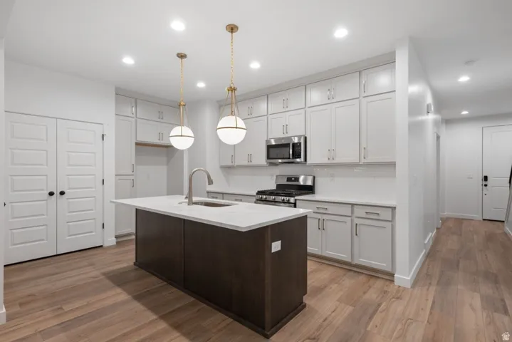 Dual tone kitchen with a center island with sink, two tone cabinetry, stainless steel appliances, dark wood-style flooring, and decorative light fixtures