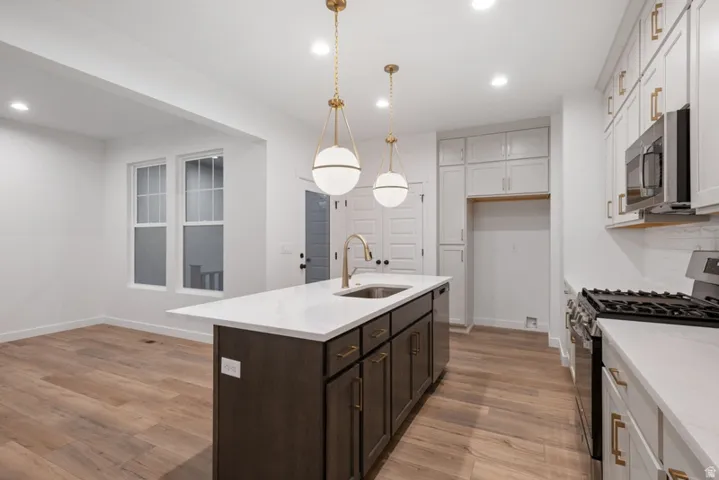Kitchen featuring stainless steel appliances, light stone countertops, a kitchen island with sink, light wood-style floors, and pendant lighting