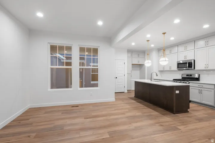 Kitchen with two tone color scheme, a center island with sink, stainless steel appliances, light wood-style floors, and decorative light fixtures