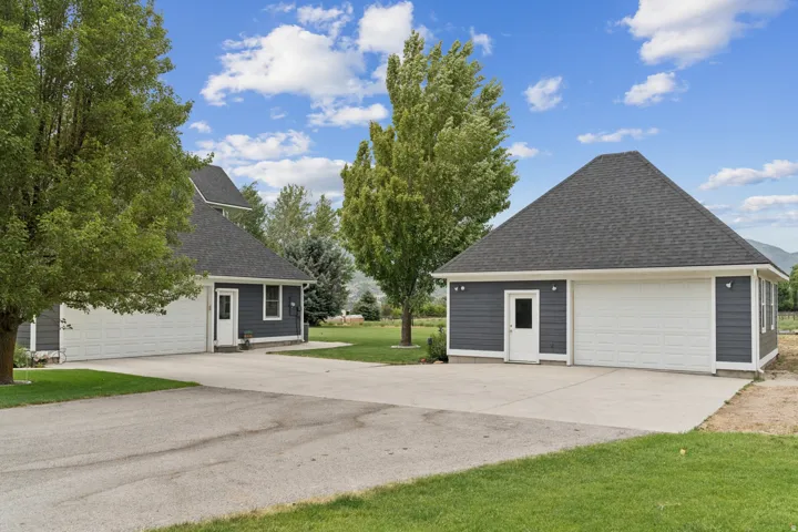View of property exterior with a shingled roof, a garage, a yard, and an outdoor structure