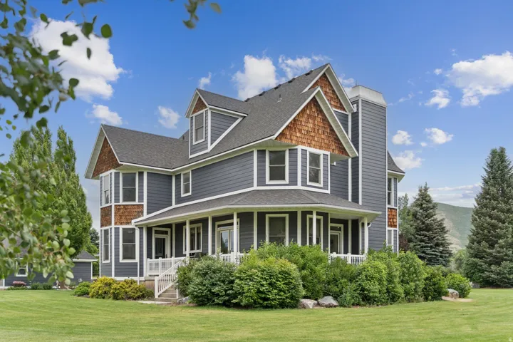 Back of house with covered porch, a lawn, and a shingled roof