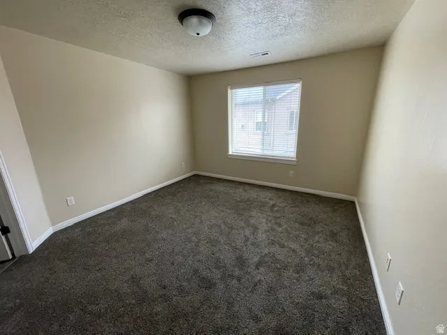 Spare room with dark carpet and a textured ceiling