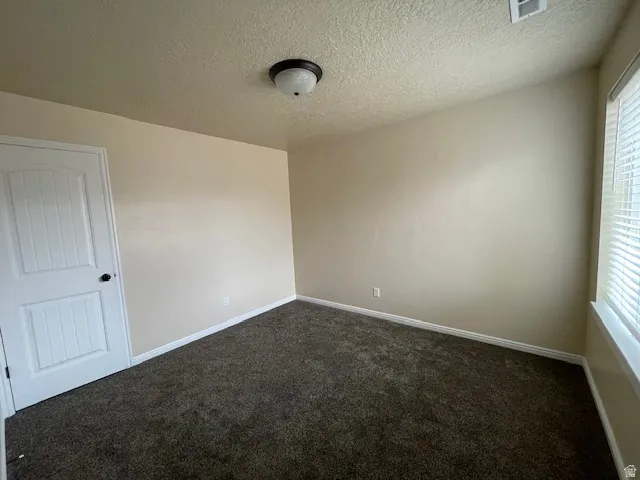 Unfurnished room featuring dark colored carpet and a textured ceiling