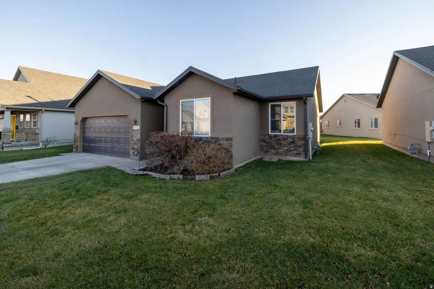 Ranch-style house featuring a front lawn, stucco siding, driveway, a garage, and stone siding